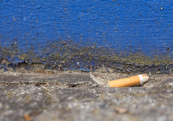 Discarded cigarette butt lying outdoors on cement paving