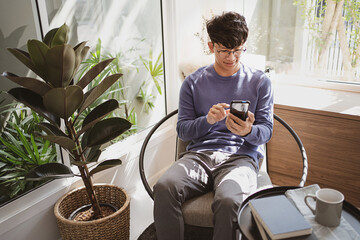 Young attractive man sitting on sofa using smart phone at home.