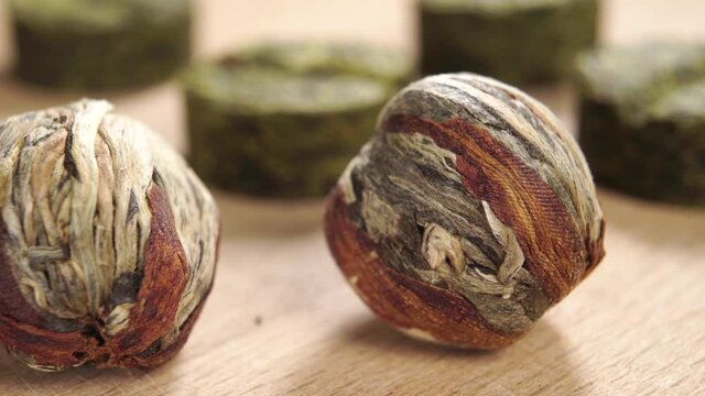 Round balls of green tea. Herbal pills of pressed dried leaves in blur. On a wooden surface. Macro. Dolly shot. Selective focus.