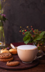 coffee with milk foam in a glass mug on a wooden table next to a bouquet of wildflowers and cookies