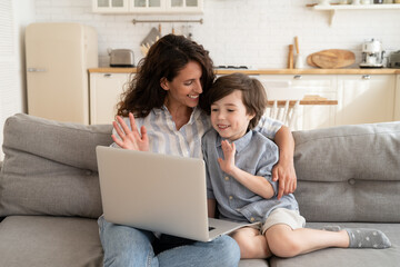 Cheerful mom and little kid make video call on laptop wave hands to computer webcam smiling to grandparents online. Happy mother and preschool son at home telecommuting with dad greeting on videocall - obrazy, fototapety, plakaty