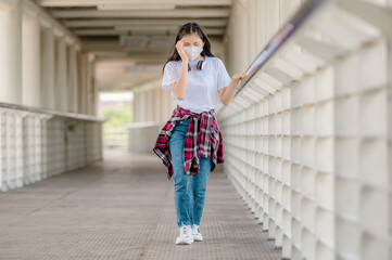 An Asian girl wearing a mask walks on an overpass with headaches, sudden fainting from debilitating conditions, and fever from coronavirus.