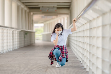 An Asian girl wearing a mask walks on an overpass with headaches, sudden fainting from debilitating conditions, and fever from coronavirus.