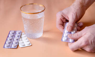 A glass of water and pills on the table. The person takes the medicine