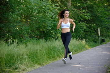 Fit woman in her 30's jogging in the park. Young woman with black trousers and white top in the park.