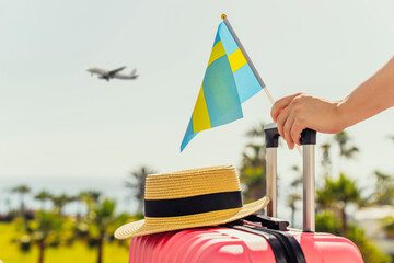 Woman with pink suitcase, hat and Sweden flag standing on passengers ladder and getting out of...