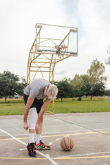 Naklejka premium Young man adjusting his knee brace on an abandoned basketball court.