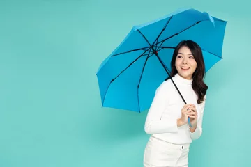 Fotobehang Young Asian woman holding blue umbella standing isolated on green background © comzeal