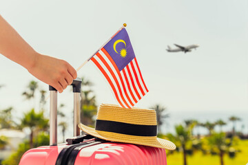 Woman with pink suitcase, hat and Malaysia flag standing on passengers ladder and getting out of...