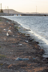 Fototapeta premium Spilled garbage on the beach of the big city. Empty used dirty plastic bottles. Dirty sea sandy shore the Black Sea. Environmental pollution. Ecological problem