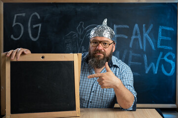 A strange guy conspiracy theorist in a protective aluminum foil hat and glasses sits at a table and...
