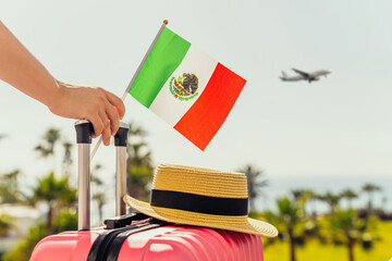 Woman with pink suitcase, hat and Mexico flag standing on passengers ladder and getting out of airplane opposite sea coastline with palm trees. - 440807885
