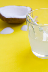 Glass with coconut water and straw on yellow background