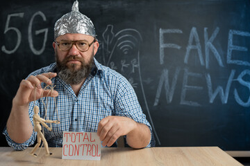 a puppet in the hands of a man in a foil hat sitting at the table. Man controls people and...
