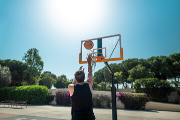 Male sportsman playing basketball throwing the ball at playground, view from behind