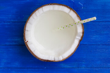 Cracked coconut with coconut water and straw on blue wooden table