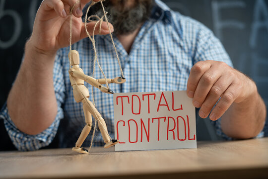 Close-up of a crafty puppet in the hands of a conspiracy theorist man sitting at the table. Man controls people and consciousness. Manipulations and total control. Fake news.