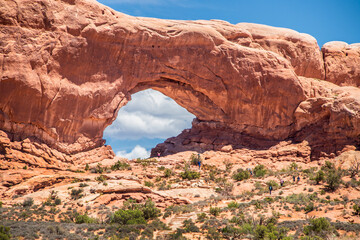Fototapeta premium Huge natural red arch at Arches National Park in Utah USA with tourists walking up rock stairs toward it.