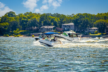 Three speedboats at lake racing in choppy water past lakeside homes and trees on nearby shore on...