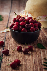 Vertical shot of fresh red cherries on a bowl with a hat on a wooden table