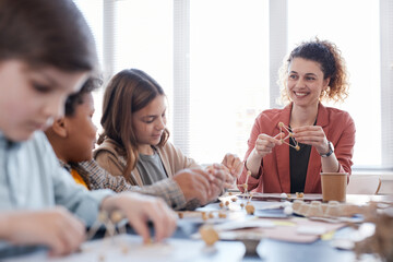 Portrait of smiling female teacher with group of children enjoying arts and crafts class in school,...