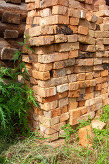 Pile of old bricks in the grass by the log wall. Vertical image.