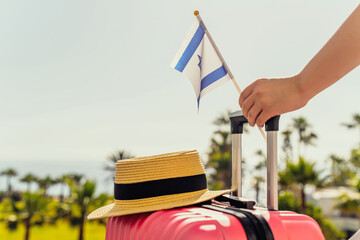 Woman with pink suitcase, hat and Israel flag standing on passengers ladder and getting out of...