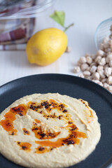 Home made hummus bowl, decorated with boiled chickpeas, lemon and olive oil over a rustic white background.