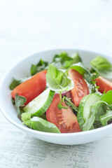 Simple Salad with Tomatoes, Cucumber and fresh Basil. Bright wooden background. Close up. Copy space. 