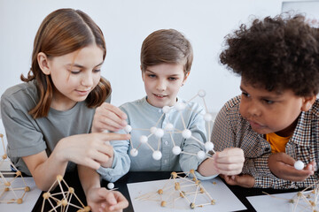 Group of three children playing with wooden models during art and craft class in school