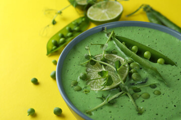 Plate of pea soup and ingredients on yellow background