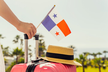 Woman with pink suitcase, hat and Panama flag standing on passengers ladder and getting out of airplane opposite sea coastline with palm trees.