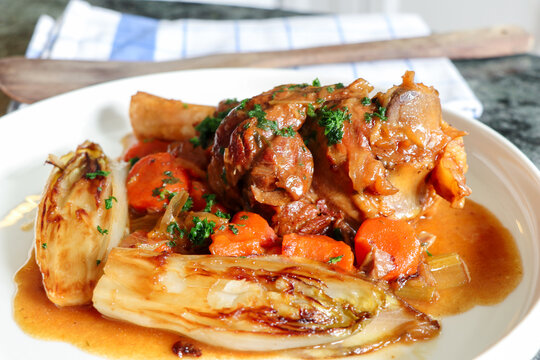 image of bone of lambs slow cooking with carrots and onions with rosemary leaves, served with gravy sauce and grilled Endives.