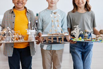 Cropped portrait of group of children holding school projects and looking at camera during art and craft lesson in school