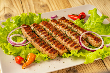 Chevapchichi, a meat appetizer on a wooden table. Lettuce leaves and hot pepper complement the meat dish. Lula-Kebab. Selective focus.