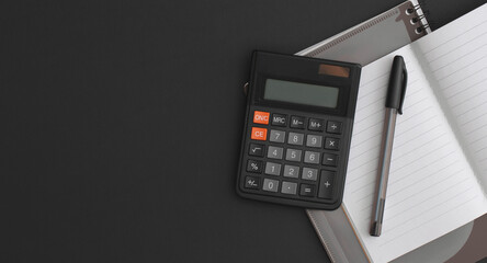 Calculator, notebook, pen on black leather background. Top view with copy space. Flat lay composition.