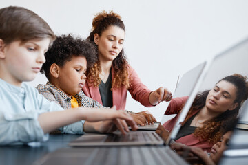 Side view portrait of young female teacher helping boy using laptop during IT class in school