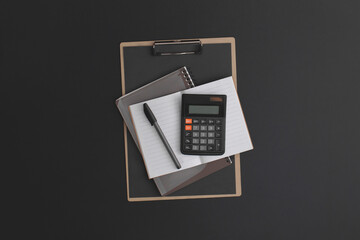 Calculator, notebook, pen on black leather background.