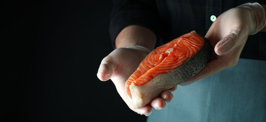 Man in gloves hold salmon meat on dark background