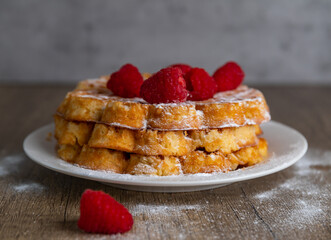Three waffles stacked, garnished with raspberriesThree waffles stacked on white plate, garnished with raspberries and powdered sugar