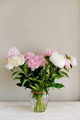 Studio shot of beautiful peony flowers in glass vase on a table over gray wall background with a lot of copy space for text. Feminine floral composition. Close up, backdrop.