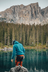 Fototapeta na wymiar closeup of person wearing blue and orange out of focus, spruce forest reflected in blue water lake and Dolomite mountain in the background