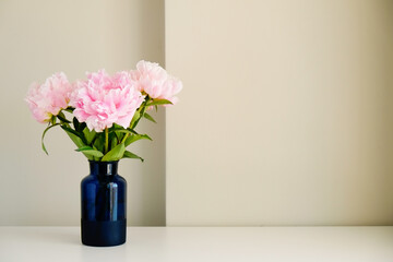 Studio shot of beautiful peony flowers in blue glass vase on a table over gray wall background with a lot of copy space for text. Feminine floral composition. Close up, backdrop.