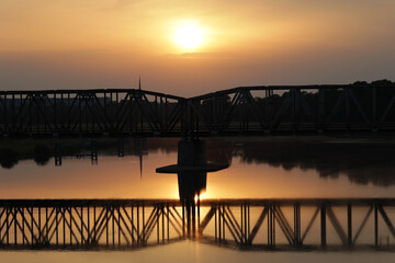 Zachód słońca nad rzeką przy moście kolejowym. 