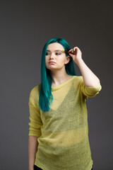 The girl artist holds a brush with paint. Woman with blue green hair in a yellow sweater isolated on a grey background. Bright colored appearance of a creative person