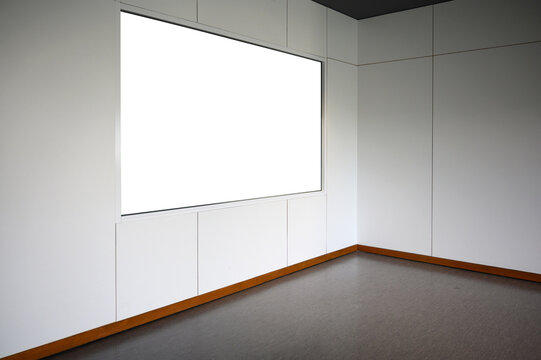 Blank white poster frame on white wall near corner room. Free space for display or montage products.