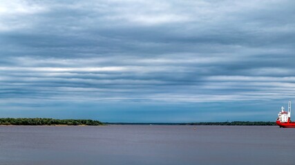 Obraz premium Cloudy sky above the water surface of a large river. Marine vessel in the roads. Northern Dvina, Arkhangelsk, Russia