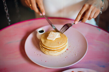 Young woman sitting at table begins to eat portion of sweet pancakes.Home-cooked meals. Recreation and travel. Proper nutrition. Taste and pleasure.