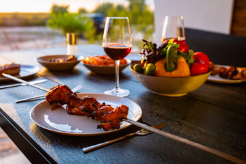 Fried meat on a skewer.Shish kebab on a plate.Skewer with a kebab and a glass of wine.Dinner on the terrace with wine and meat.Fried meat for dinner.Meat.Covered dinner.Delicious food.Summer