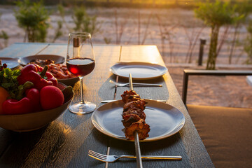 A glass of wine with grilled meat on the summer terrace.A glass of wine at sunset with dinner in the summer.Picnic.Dinner on the street with wine.Meat on a skewer with salad.Mediterranean diet.Summer 